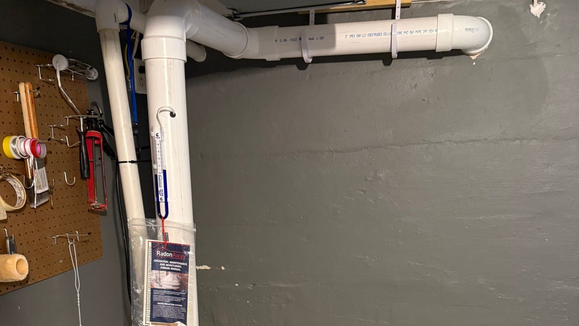 Radon mitigation system installed by Eagle Air, with the PVC vent pipe, pressure gauge, and system label in a basement