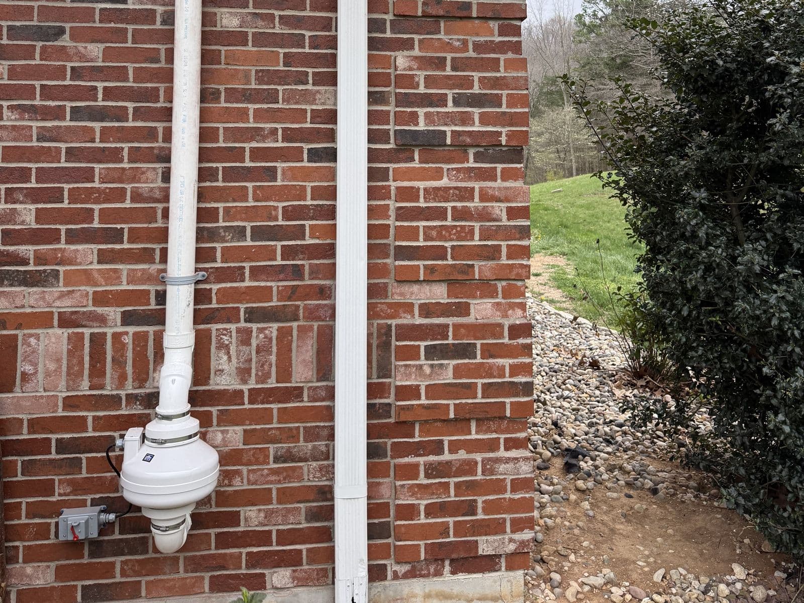 Radon mitigation system fan and vent pipe on a brick home exterior
