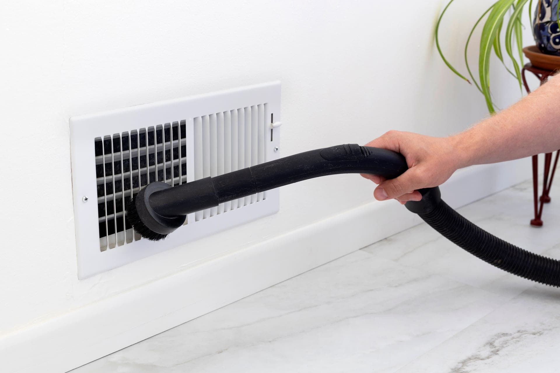 Vacuum hose cleaning a floor air register in a Missouri home